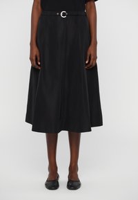 Svart knälång kjol med cirkulär silverfärgad spännbälte. Tillverkad av slätt tyg med en lätt glans och midja med rynk för komfort.