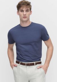 T-paita, jossa on lyhyet hihat ja tummansininen väri, valmistettu pehmeästä kankaasta, yhdistetty vaaleanvärisiin pellavahousuihin ja ruskeaan punottuun vyöhön.