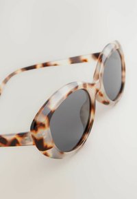 Lunettes de soleil en écaille de tortue avec des verres ronds surdimensionnés ; monture en plastique léger avec des verres polarisés foncés et une texture lisse.