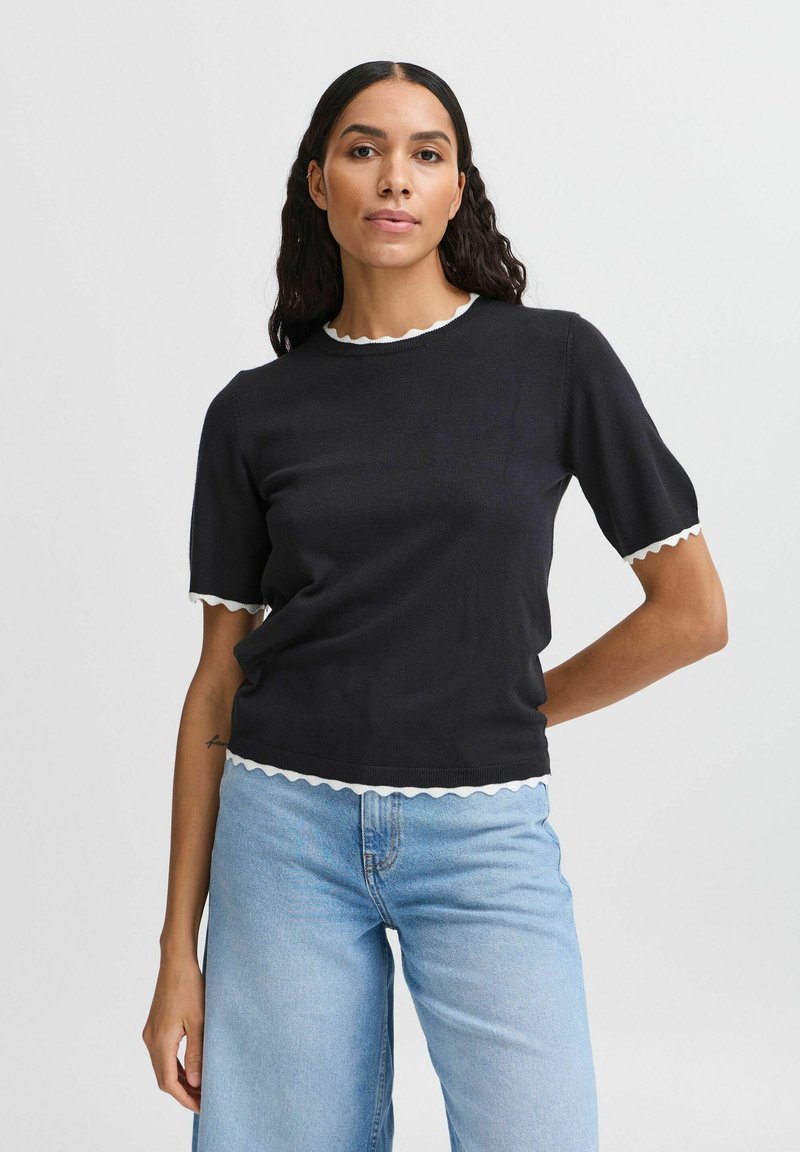 Sort striktrøje med korte ærmer og bølget hvid kant ved halsudskæringen og kanten. Sammen med lyseblå vide jeans.