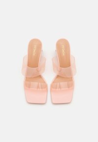 Paire de sandales à talons hauts roses avec bouts carrés et larges brides transparentes, vue de dessus sur fond blanc.