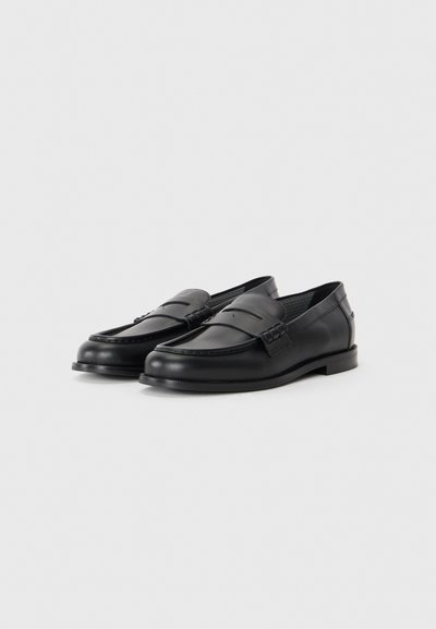 Svarta läderloafers med rund tå, dekorativ sömnad och en låg, platt sula. Har en slät yta och minimala detaljer.