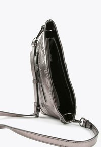 Metalna srebrna crossbody torba s urezanim uzorkom, otvorenim gornjim zatvaračem koji otkriva crni unutrašnjost, i podesivim remenom s metalnim kopčama.