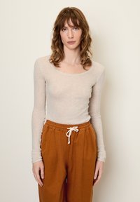 Svetlo béžový dlhý rukáv s výstrihom do lode skombinovaný s voľným strihom, hrdzavo sfarbenými nohavicami s viazacím pásom.