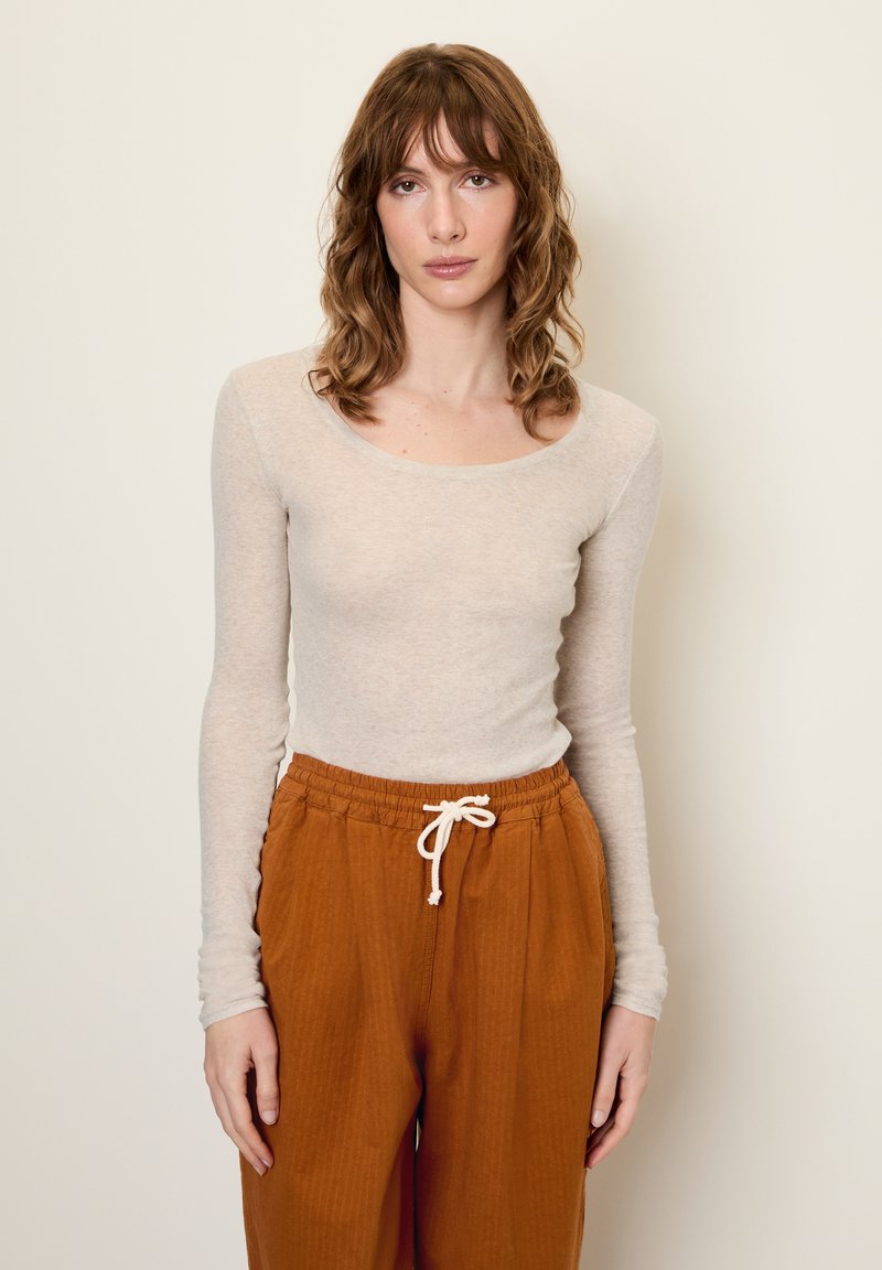 Svetlo béžový dlhý rukáv s výstrihom do lode skombinovaný s voľným strihom, hrdzavo sfarbenými nohavicami s viazacím pásom.