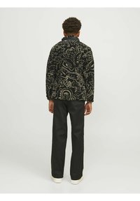 Černý vzorovaný sakou s texturovaným povrchem, které má paisley design a klasický límec, spárované s černými kalhotami a bílými botami.