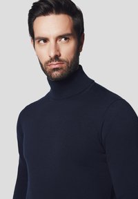 Granatowy sweter z golfem, wykonany z cienkiej dzianiny, charakteryzujący się dopasowanym krojem i prążkowanym kołnierzem, na neutralnym tle.