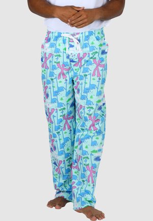 Person trägt hellblaue Pyjamahose mit bunten Dinosaurier- und Pflanzenmustern, steht barfuß mit vor der Brust verschränkten Händen.