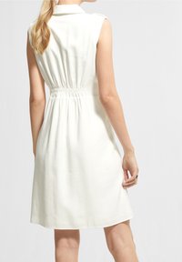 Robe blanche sans manches avec un col, taille cintrée et texture douce. Jupe évasée atteignant le mi-cuisse, avec un detailing minimal.