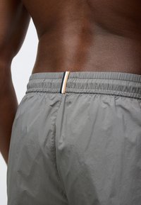 Τα γκρι αθλητικά σορτς διαθέτουν ελαστική μέση με ένα λεπτό μαύρο και πορτοκαλί διακοσμητικό ρίγες. Το ύφασμα φαίνεται ελαφρύ και με υφή.