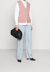 Canotta rosa a righe con bottoni, camicia bianca sotto, jeans larghi azzurri chiari e borsa nera a sacco. Tacchi neri a punta.