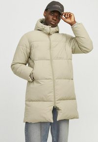 Lys beige pufferjakke med hætte, lynlås og store quiltede sektioner. To sidelommer og elastiske manchetter. Kombination med lys denim.
