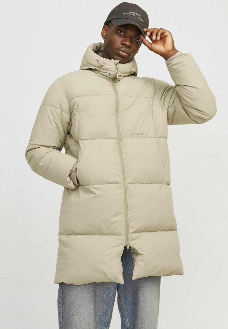 Lys beige pufferjakke med hætte, lynlås og store quiltede sektioner. To sidelommer og elastiske manchetter. Kombination med lys denim.