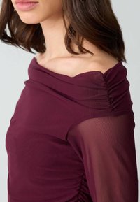 Bordeauxfarbene Schulterfreie Bluse mit gerafften Ärmeln, ausgestattet mit transparenten Stoffdetails und glatter Textur. Entworfen für eine figurbetonte Silhouette.