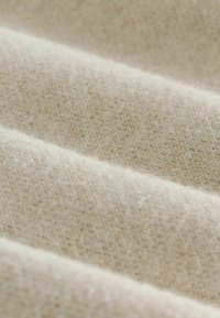 Beež värviga kootud kangas, millel on pehme, tekstuuriga pind, mis näitab nõrku värvimuutusi ja õrna soonilist mustrit.