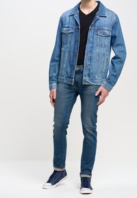 Světlemodrá džínová bunda s předním zapínáním na knoflíky a dvěma náprsními kapsami; kombinováno s tmavými džíny a námořnickými vysokými teniskami.