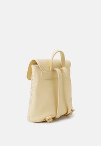 Zaino giallo in ecopelle con superficie liscia, pattina arrotondata, spallacci regolabili e dettagli decorativi perforati sui lati.