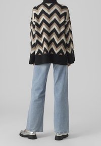 Przesadny sweter w wzór zygzaka w odcieniach beżu, czerni i bieli, w połączeniu z jasnoniebieskimi spodniami typu wide-leg i srebrnymi butami na platformie.