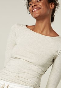 Top de manga larga gris claro con un amplio escote barco, textura suave, corte ajustado y un sutil patrón jaspeado. Coordinable con pantalones casuales.