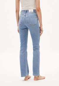 Vaaleansiniset farkut suoralla lahkeella, näkyvillä takataskuilla ja korkealla vyötäröllä. Kangas on hieman teksturoitu ja haalistunut.