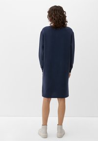 Mörkblå midiklänning med långa ärmar, tillverkad av ett mjukt tyg. Har en avslappnad passform och sidoöppningar, tillsammans med ljusa ankelstövlar.