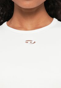 Vit kortärmad skjorta med rund halsringning och en liten broderad logotyp i oval form i mitten. Slät textur.