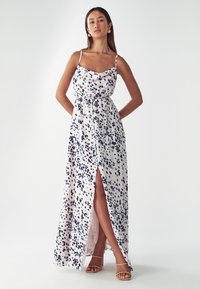 Robe maxi en tissu avec une base rose et un motif éclaboussé bleu marine. Présente des bretelles spaghetti et une fente à l'avant. Texture lisse.
