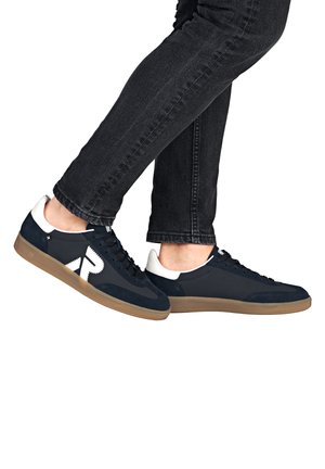 Baskets en daim bleu marine avec des accents blancs et une semelle en caoutchouc beige. Elles présentent un design à lacets et un logo bien visible sur le côté.