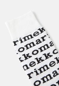 Valged puuvillased sokid, millel on korduv musta trükitud teksti muster. Ülemisel osal on sooniline äär, mis annab tekstuurse viimistluse.