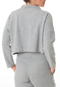 Pull en maille gris, raccourci, avec une finition texturée et une coupe décontractée. Manches longues, sans attaches visibles, porté sur un pantalon gris assorti.