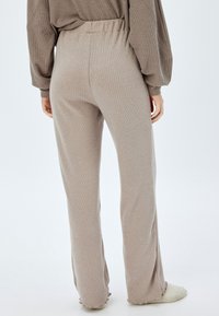 Pantalones beige de tejido acanalado, ligeros, con cintura elástica, piernas acampanadas y detalles de dobladillo sin terminar, combinados con una blusa de gran tamaño.