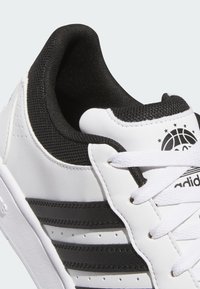 Białe sportowe sneakersy z czarnym siateczkowym wnętrzem, czarnymi paskami i teksturowaną skórą. Posiadają białe sznurówki i logo z boku.