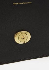 Portefeuille en cuir pleine fleur noir avec une fermeture à matériel circulaire doré, présentant une texture lisse et un surfilage contrastant le long des bords.