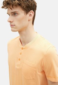 Kortærmet, lys orange henley skjorte lavet af blød bomuld med rund hals, fire-knap placket og en enkelt brystlomme.