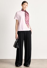 Ροζ βαμβακερό t-shirt με λογότυπο, συνδυασμένο με φαρδιά μαύρη παντελόνα. Διακρίνεται για ένα μοτίβο μωβ φουλάρι και μια μικρή μαύρη τσάντα.