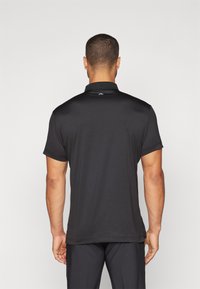 Polo nero con colletto piatto, maniche corte e texture liscia. Presenta un piccolo logo vicino all'area del collo.