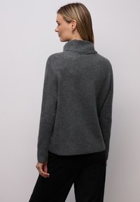 Grå strikket sweater med høj krave, ribbet manchetter og kant. Blød tekstur, afslappet pasform og minimale sømme for et rent design.