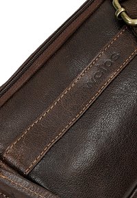Bruine leren tas met een ruwe uitstraling, voorzien van een messingen rits en oranje stiksels. Logo in de zijkant geperst.