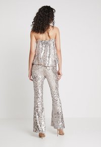 Silverfärgad paljettoutfit med vida byxor och en lös topp med tunna band, som visar en glansig, texturerad yta.