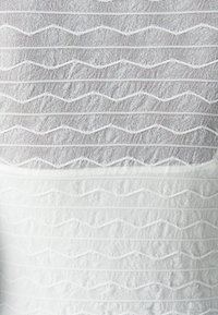 Tecido branco com costura texturizada zigzag horizontal, criando padrões ligeiramente elevados por toda a superfície.
