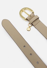 Beiger Leder Gürtel mit einer goldfarbenen rechteckigen Schnalle und einem kleinen Anhänger mit geprägter Schrift. Glatte Textur mit genähten Kanten.