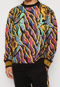 Färggad sweatshirt med ett livfullt abstrakt mönster i lila, svart och gult, med svarta ribbade mudd och fåll.