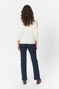 Cremefarvet sweater med trekvartærmer parret med mørkeblå flagrende jeans. Outfittet har et simpelt, rent design og tekstureret stof.