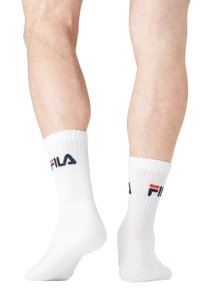 Chaussettes en coton blanches de type crew avec une texture côtelée, arborant un logo FILA tricoté bleu et rouge à la cheville. Conçues pour le confort et un bon maintien.