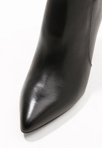 Stivaletto alla caviglia in pelle nera con punta appuntita, texture liscia e design minimalista. Caratterizzato da una tomaia senza cuciture e una silhouette elegante.