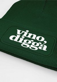 Dark green knit beanie with a rectangular white patch featuring the text "vino, diggà". Text is bold and prominent against the fabric.