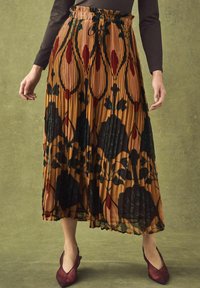 Pleated midi skirt made of fabric in warm brown with floral patterns in deep green and red. Features an elastic waistband with a tie.
