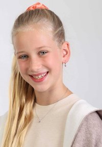 Zilveren ketting met een kleine paarse hanger; meisje met lang blond haar vastgebonden in een roze scrunchie; draagt een beige trui en een bruine cardigan.