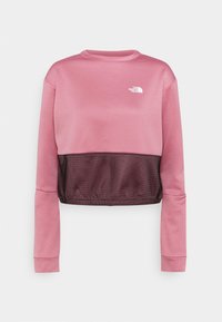 Różowy krótki sweatshirt z długimi rękawami, czarną siateczkową wstawką na dole i białym logo "The North Face" na klatce piersiowej.