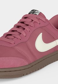 Ροζ αθλητικό παπούτσι Nike με λευκό λογότυπο Swoosh, παχιά καφέ σόλα και υφασμάτινη υφή, με κορδόνια και επενδυμένο γιακά.